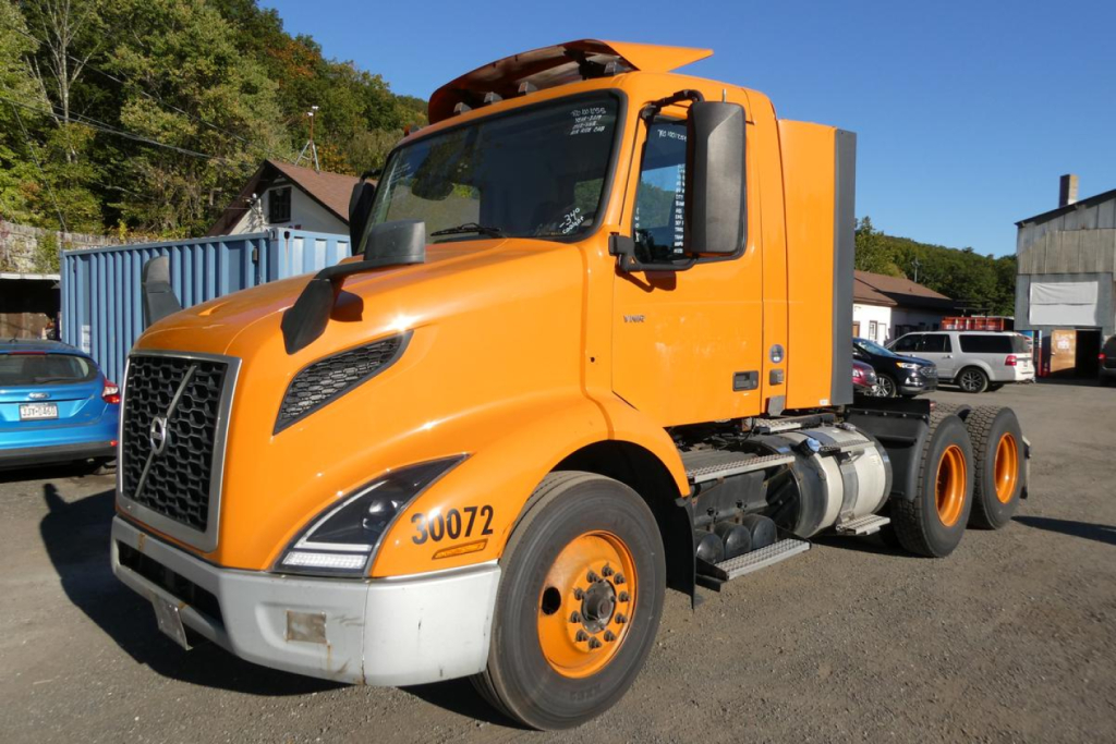Orange Volvo VNR64T300 daycab truck front-left view showing cab, grille, headlights, and front tires with stock number 30072 visible on fender.