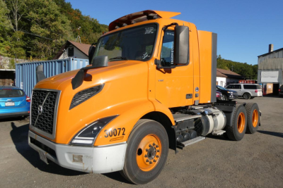 Orange Volvo VNR64T300 daycab truck front-left view showing cab, grille, headlights, and front tires with stock number 30072 visible on fender.