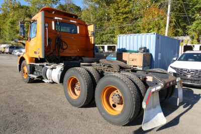 Volvo VNR64T300 truck chassis with orange cab and dual rear axles, viewed from side, showing tires and rear mud flaps.