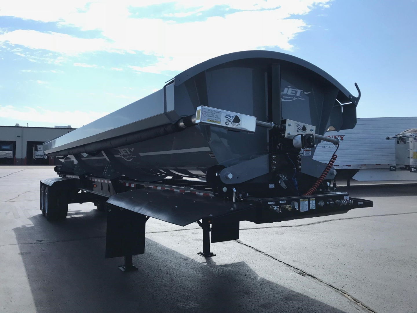 Jet Air Ride Side Dump trailer in steel gray with hydraulic hoses and rear hitch. Side view showing undercarriage and support legs.
