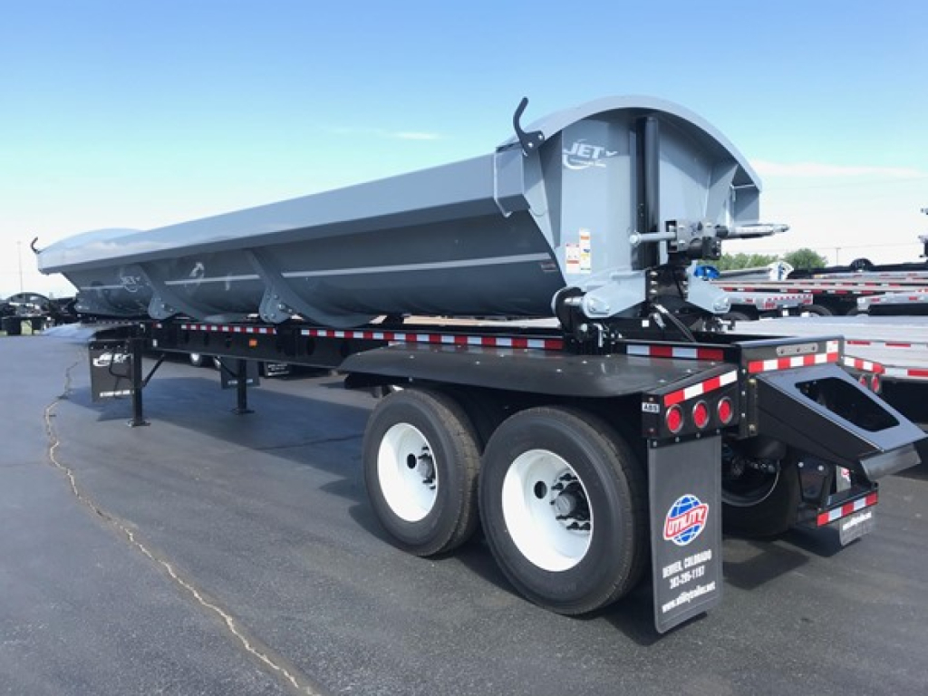 Jet air ride side-dump trailer showing dual rear axles and gray dump body with 'JET' branding on the front left side and reflective safety stripe.