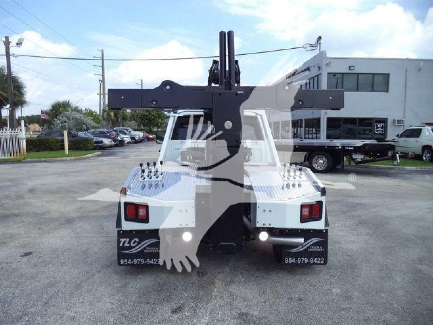 Back view of a 2024 Ram 5500 SLT tow truck with a large winch/mounting apparatus and bumper lights. Visible text includes two contact numbers on the rear bumper: 954-979-9422 repeated, and a partial 'TLC' branding on the left bumper.