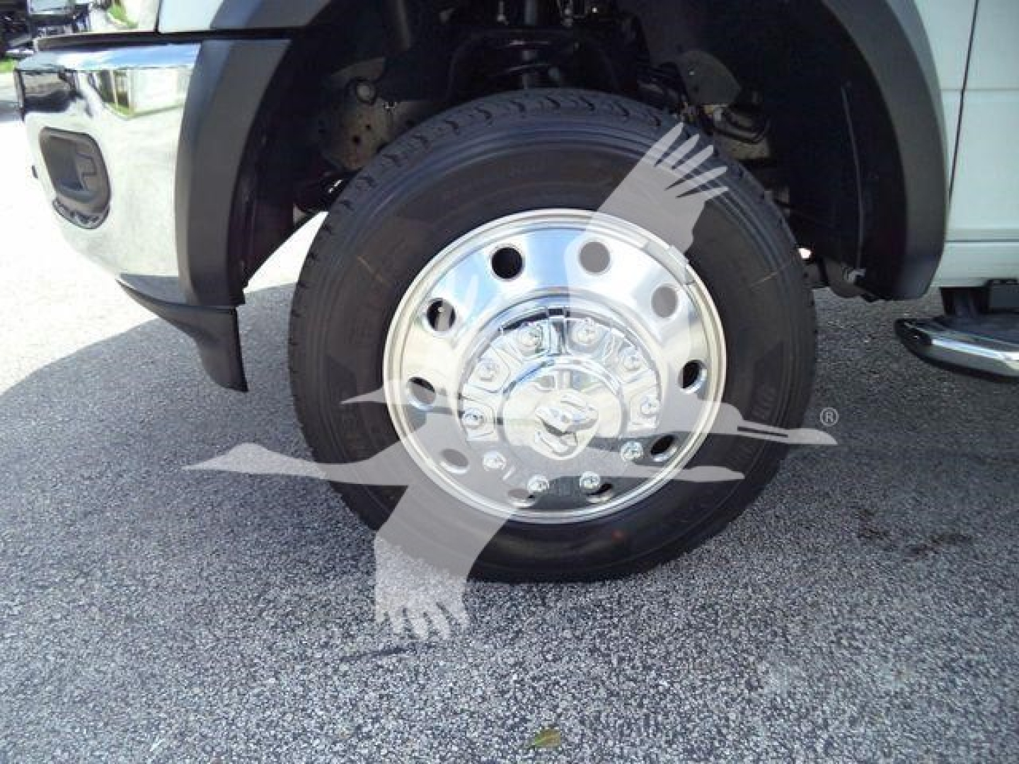 Ram 5500 front wheel and chrome hubcap, partial fender, tire tread and suspension components visible on a light-colored truck.