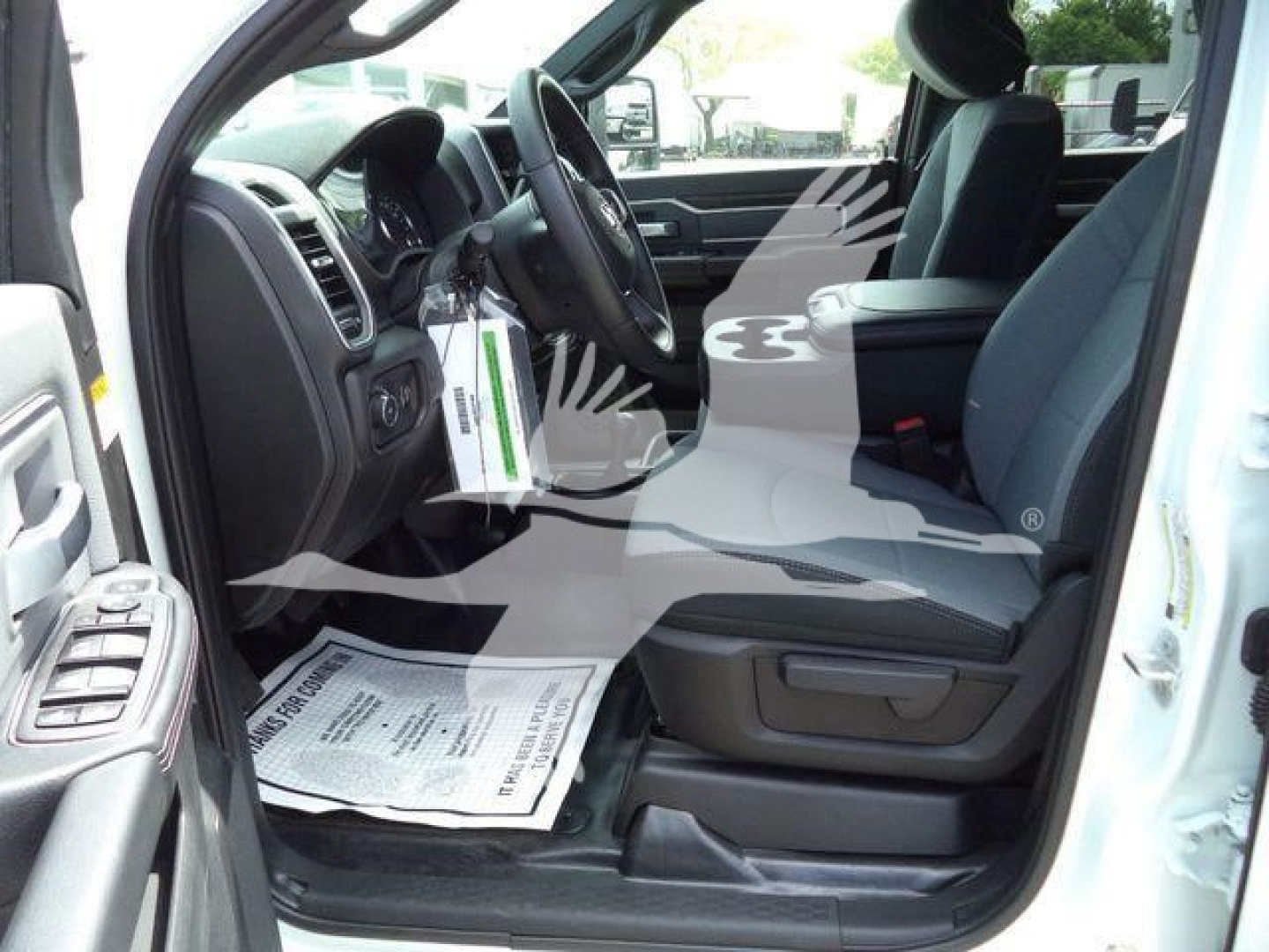 Ram pickup truck interior showing driver side with steering wheel, dashboard, front seats, and floor mat. Visible papers or tags hang from the steering column.