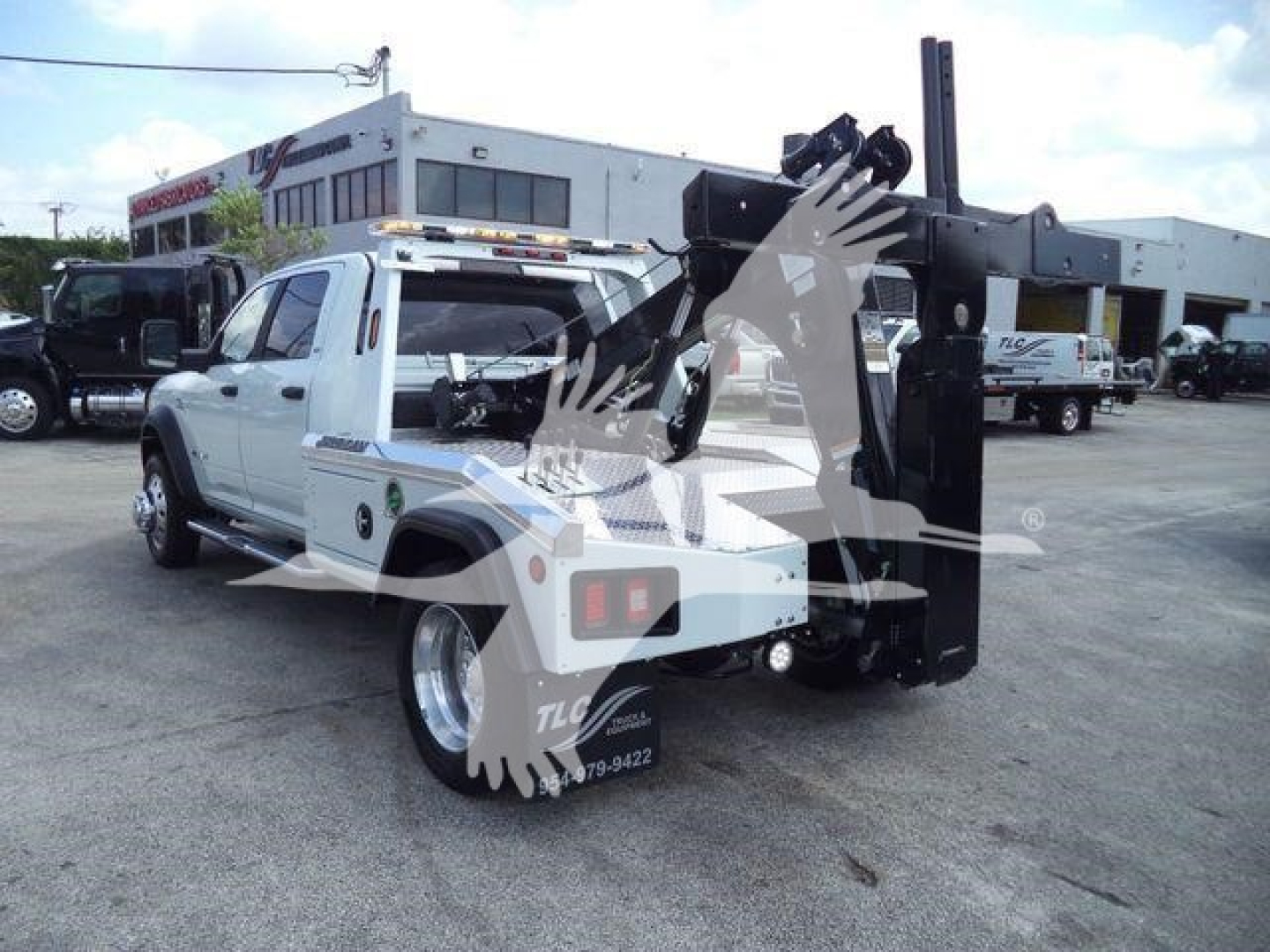 Ram 5500 SLT tow truck with a hydraulic crane/boom in rear, white cab, black equipment, in a dealership lot.