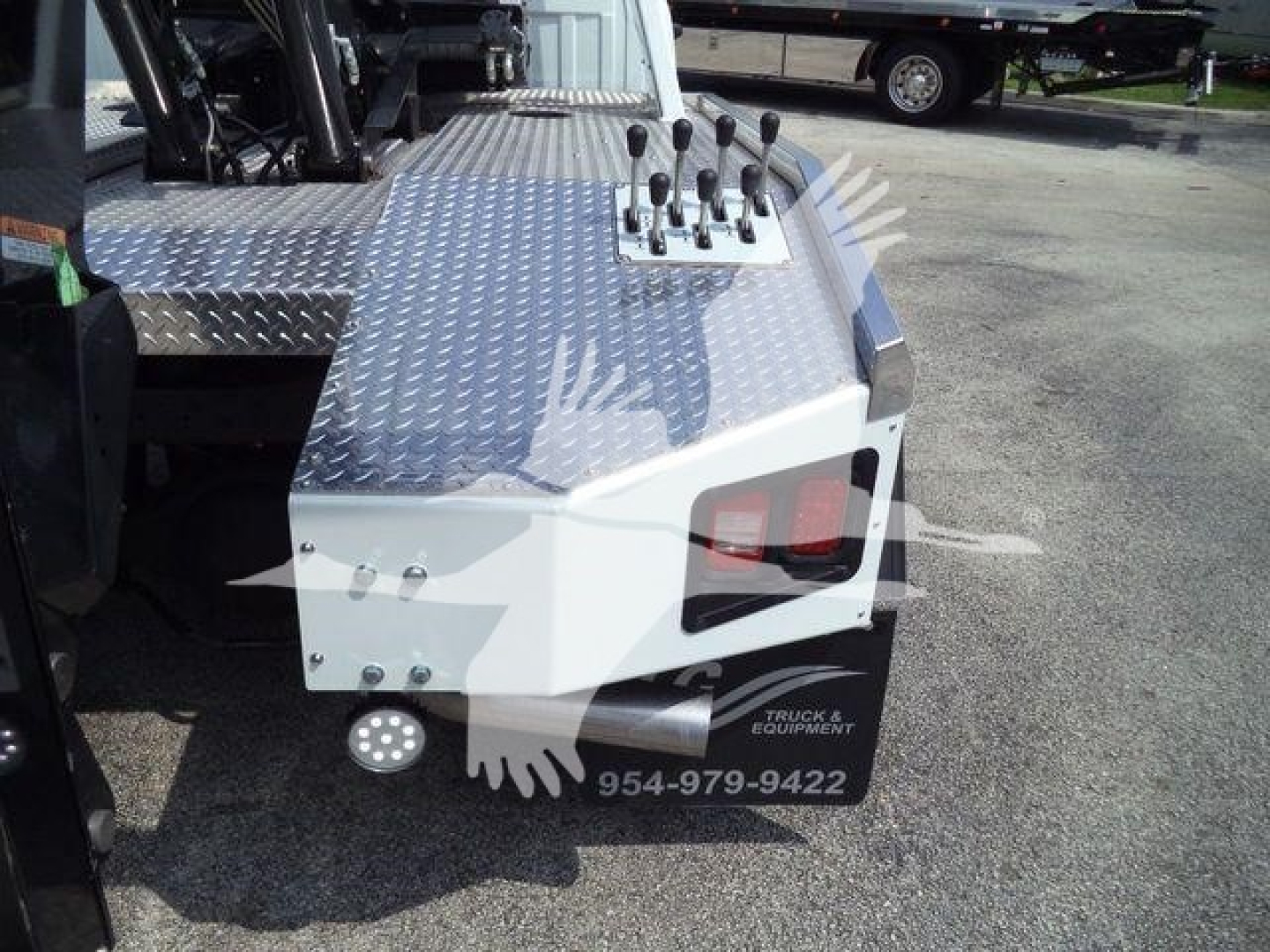 Ram 5500 winch truck rear with diamond plate deck, control levers, and a bumper with logo and phone number.