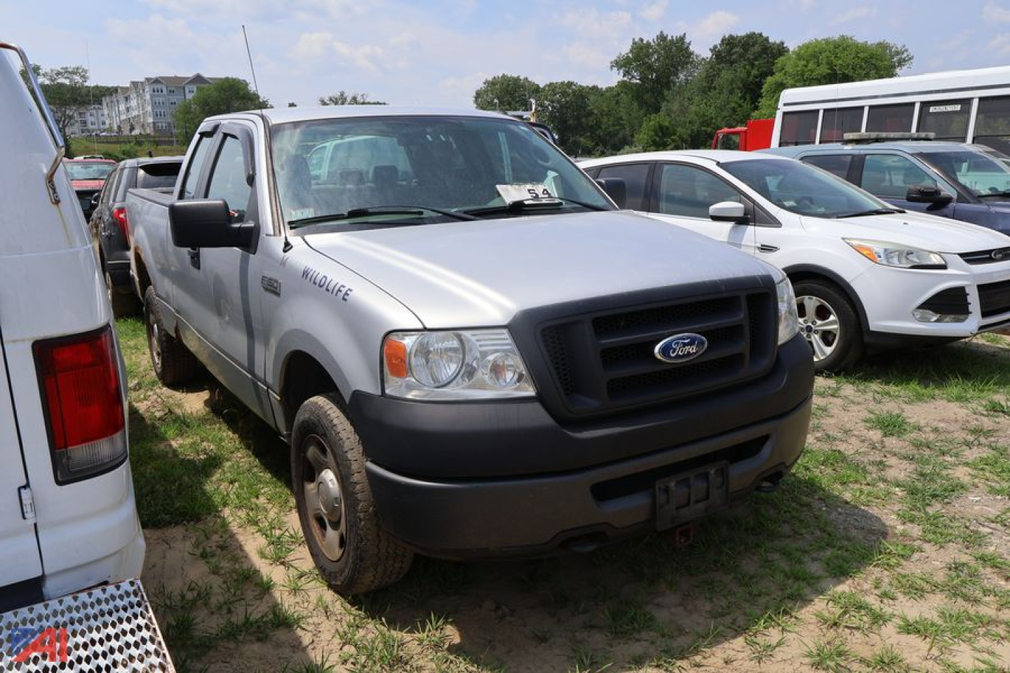 Ford F-150 pickup truck front-left view showing grille with Ford emblem and bumper; silver body with black front bumper and side mirrors; other vehicles in background.