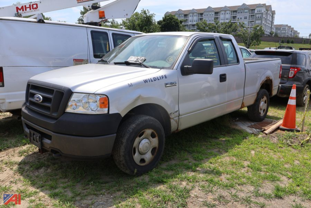 Ford F-150 pickup truck with extended cab, white exterior, badge reads ‘Wildlife’ on driver’s side, in a grassy lot with other vehicles.