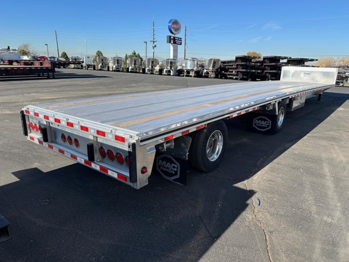 Flatbed trailer showing aluminum drop deck with multiple axles and MA C brand mud flaps.