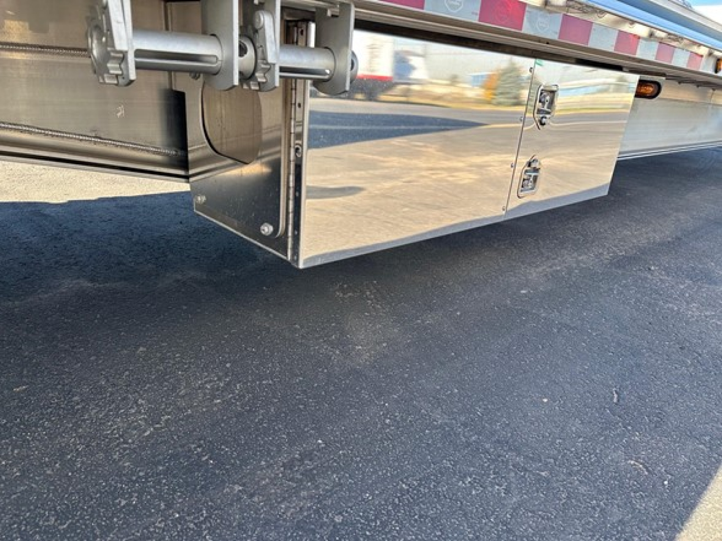 Trailer undercarriage showing polished aluminum drop deck with storage toolbox and mounting hardware