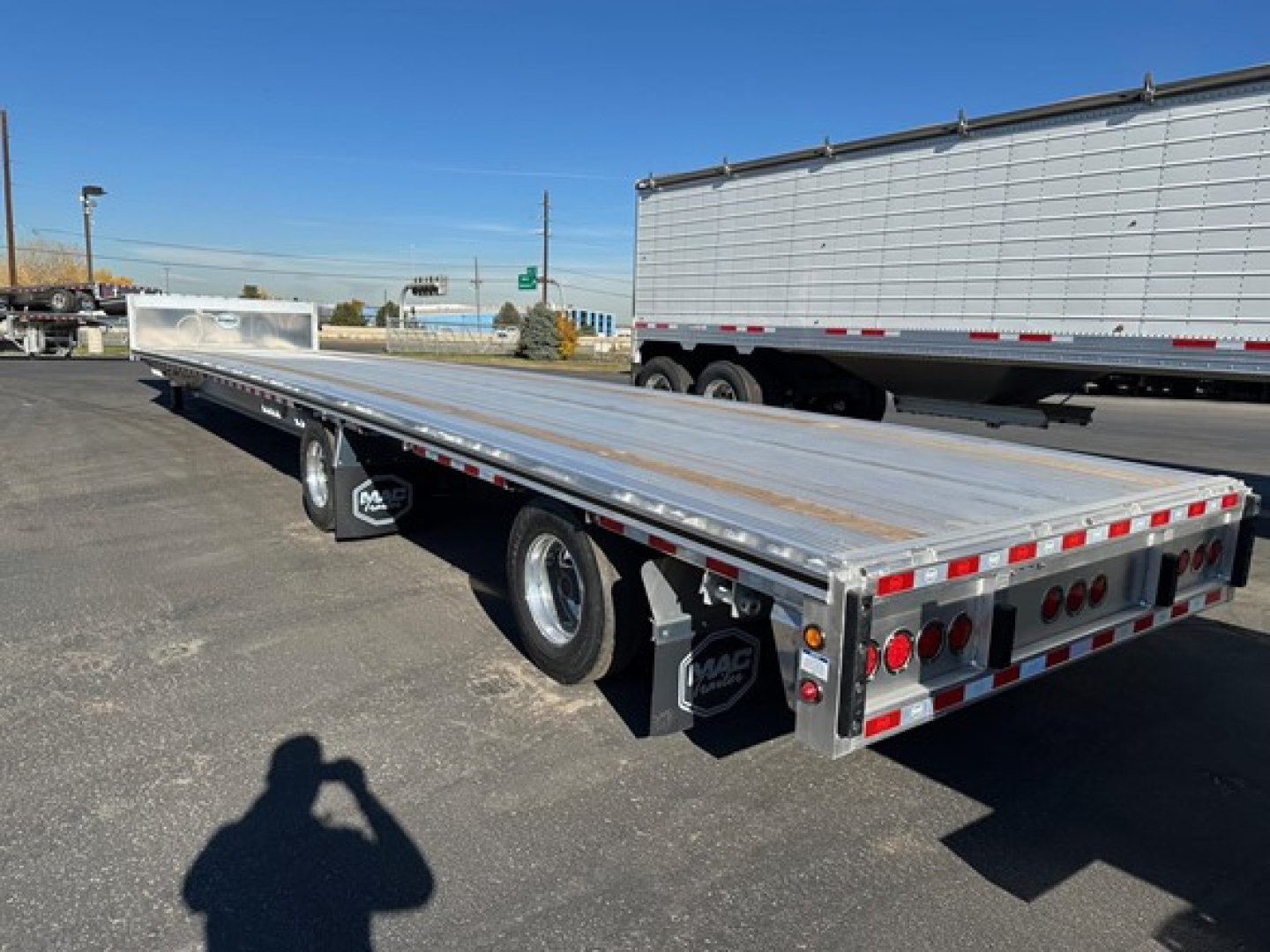 Flatbed trailer with aluminum deck and rear lighting showing drop deck trailer design and dual rear wheels.