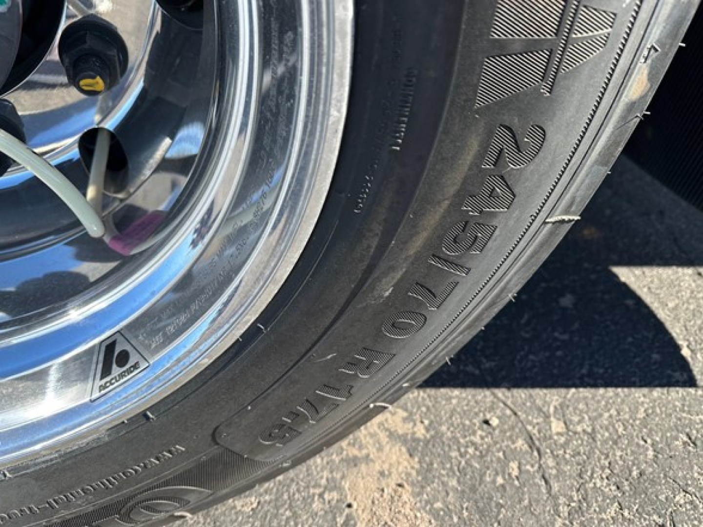 Tire and wheel close-up on a Mac drop deck trailer showing tire markings and chrome rim.