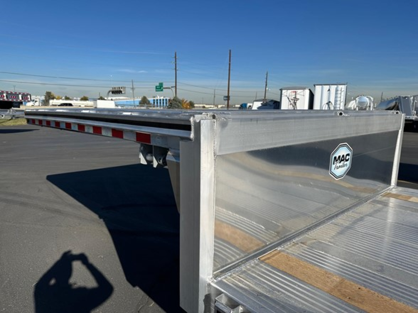 Mac drop deck trailer with aluminum bed and MAC Trailers logo on the side, edge rails visible, clear sky.