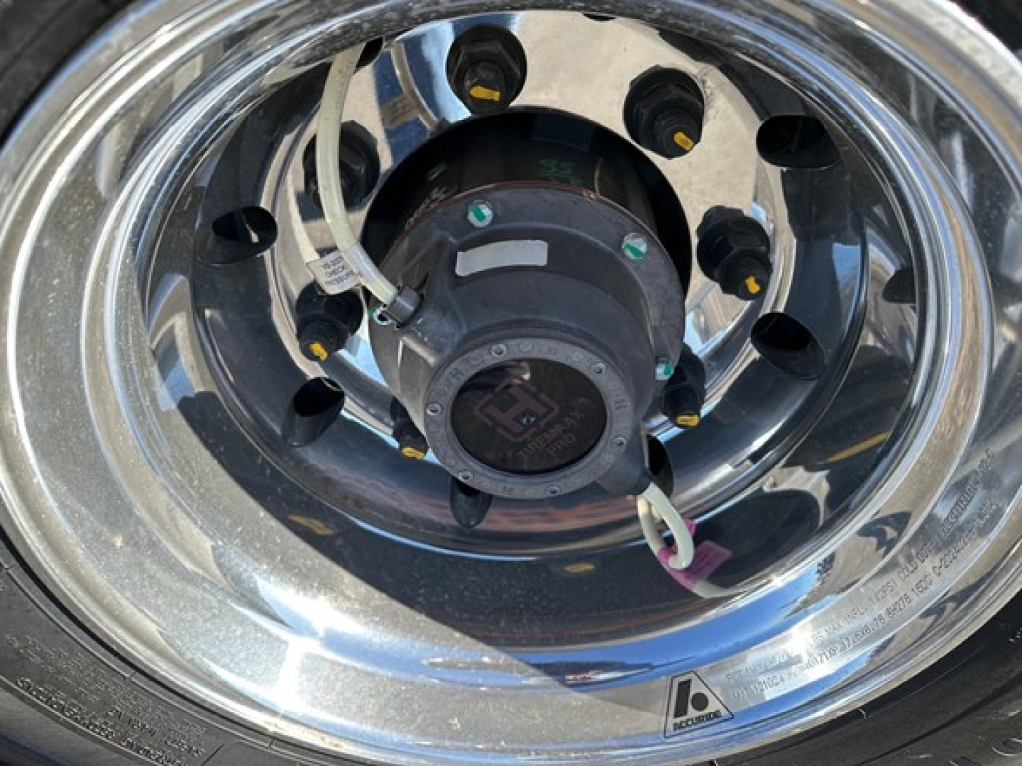 Wheel hub with chrome rim and hub accessory showing electrical connector and labels on a Mac drop deck trailer wheel assembly.