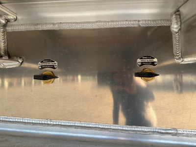 Mac All Aluminum Drop Deck trailer interior showing two black toggle handles labeled Suspension Dump and Angle Slider with metal wall and welded seams.
