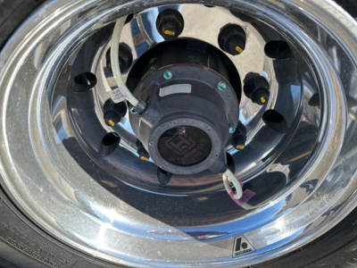 Wheel hub area of a Mac all-aluminum drop deck trailer showing chrome rim, hub assembly, and attached hoses/wires.