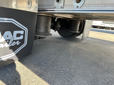 Trailer undercarriage showing dual axles and air suspension on a Mac drop deck trailer, with MAC logo mudflap in foreground.