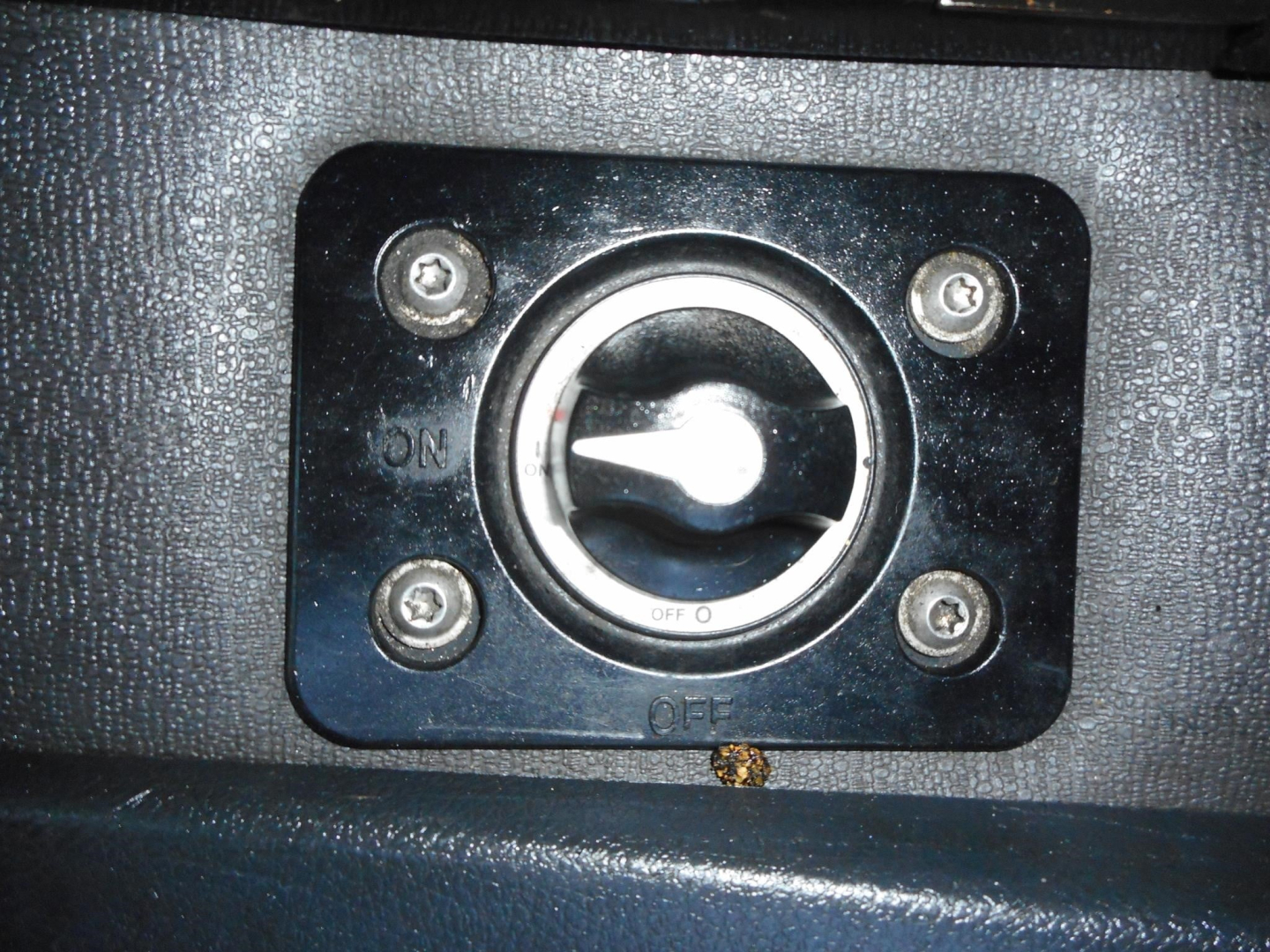 Truck interior image showing an access port with a circular dial and four screws, black frame, textured surface.