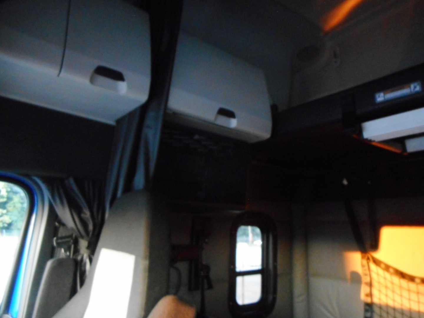 Cab interior of a Freightliner Cascadia showing overhead storage compartments and a view toward the sleeper area.