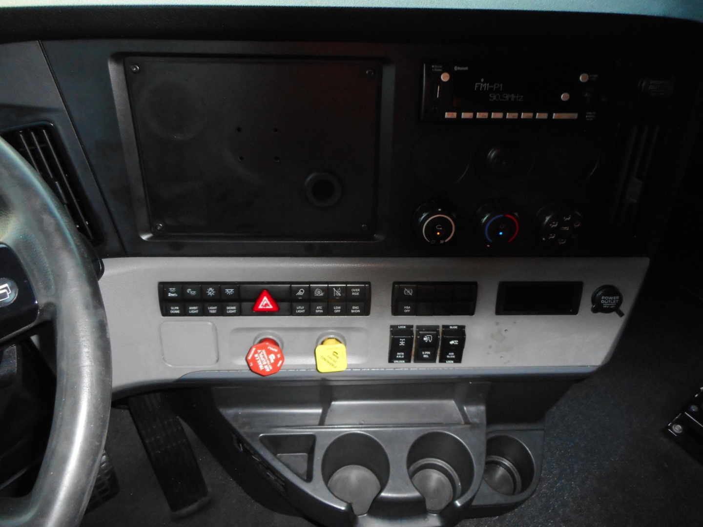 Cascadia truck dash panel showing control switches, cup holders, and dashboard gauges.