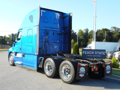 Truck cab side and rear showing blue Freightliner Cascadia sleeper with stretched cab and dual rear axles in a dealership lot.