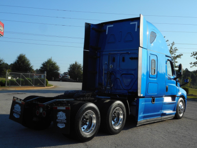 Truck cab showing 2022 Freightliner Cascadia 126 sleeper with blue exterior in a parking lot, rear view with dual rear axles and fifth wheel area visible.