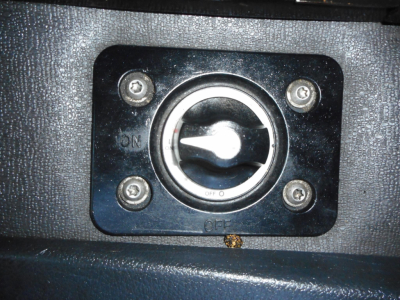 Truck interior image showing an access port with a circular dial and four screws, black frame, textured surface.