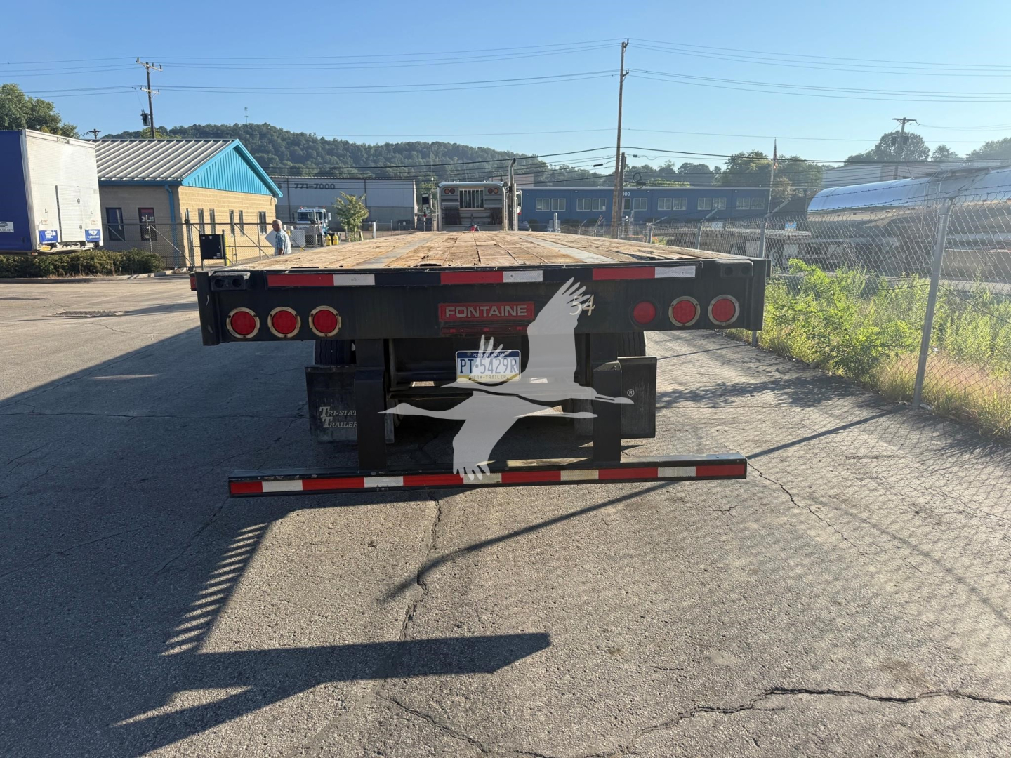 Rear view of Fontaine flatbed trailer showing Fontane logo and multiple taillights; visible license plate area and rear bumper with reflective tape.