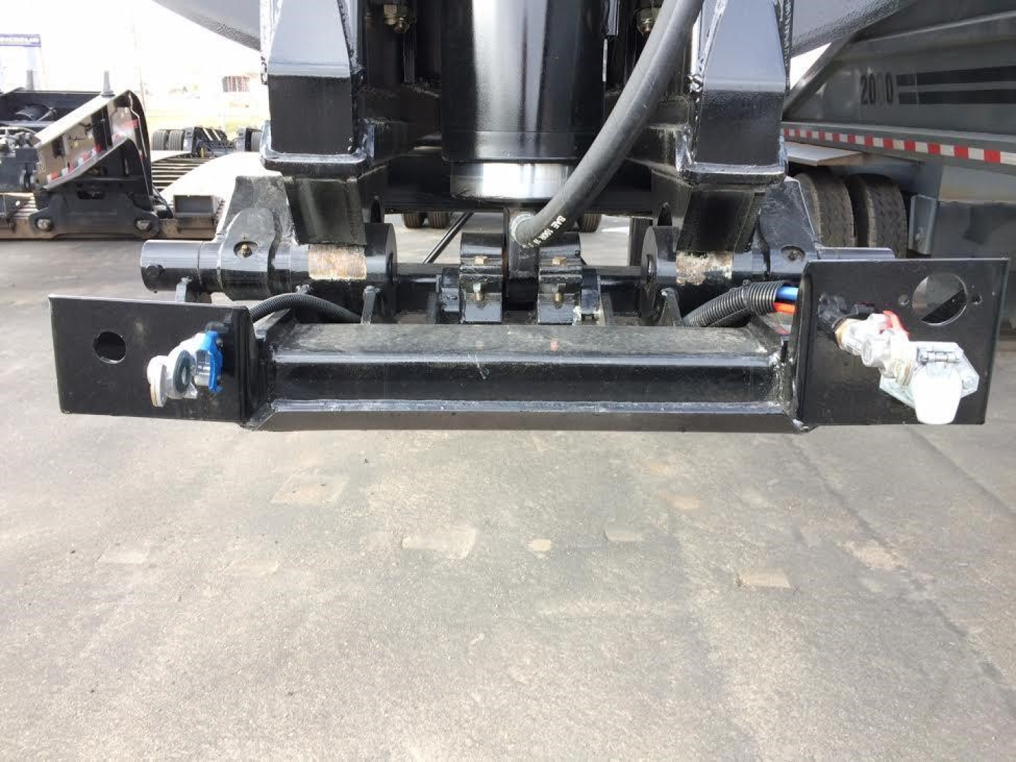 Dump trailer hitch/brackets and hydraulic components showing receiver bar and wiring mounts under a new trailer. Visible metal frame, hoses, and fittings.