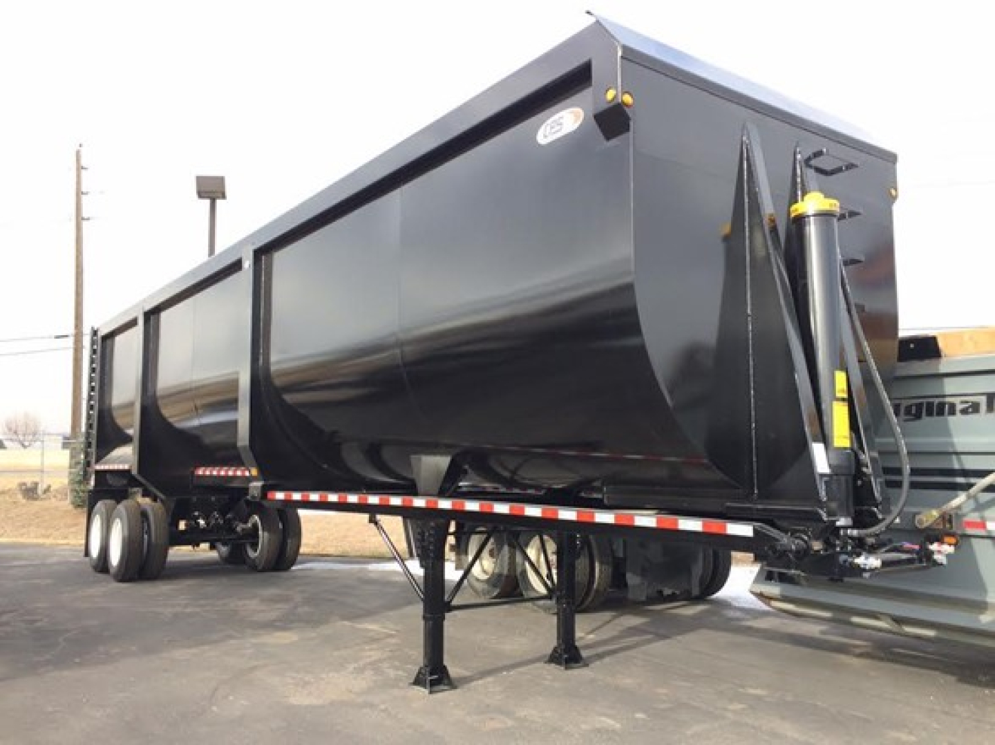 Dump trailer with black steel body and tandem axles, semi-truck hitch, and landing gear showing on a paved lot.