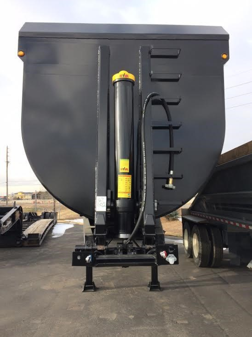 Dump trailer hitch system viewed from rear showing hydraulic cylinder and frame components.