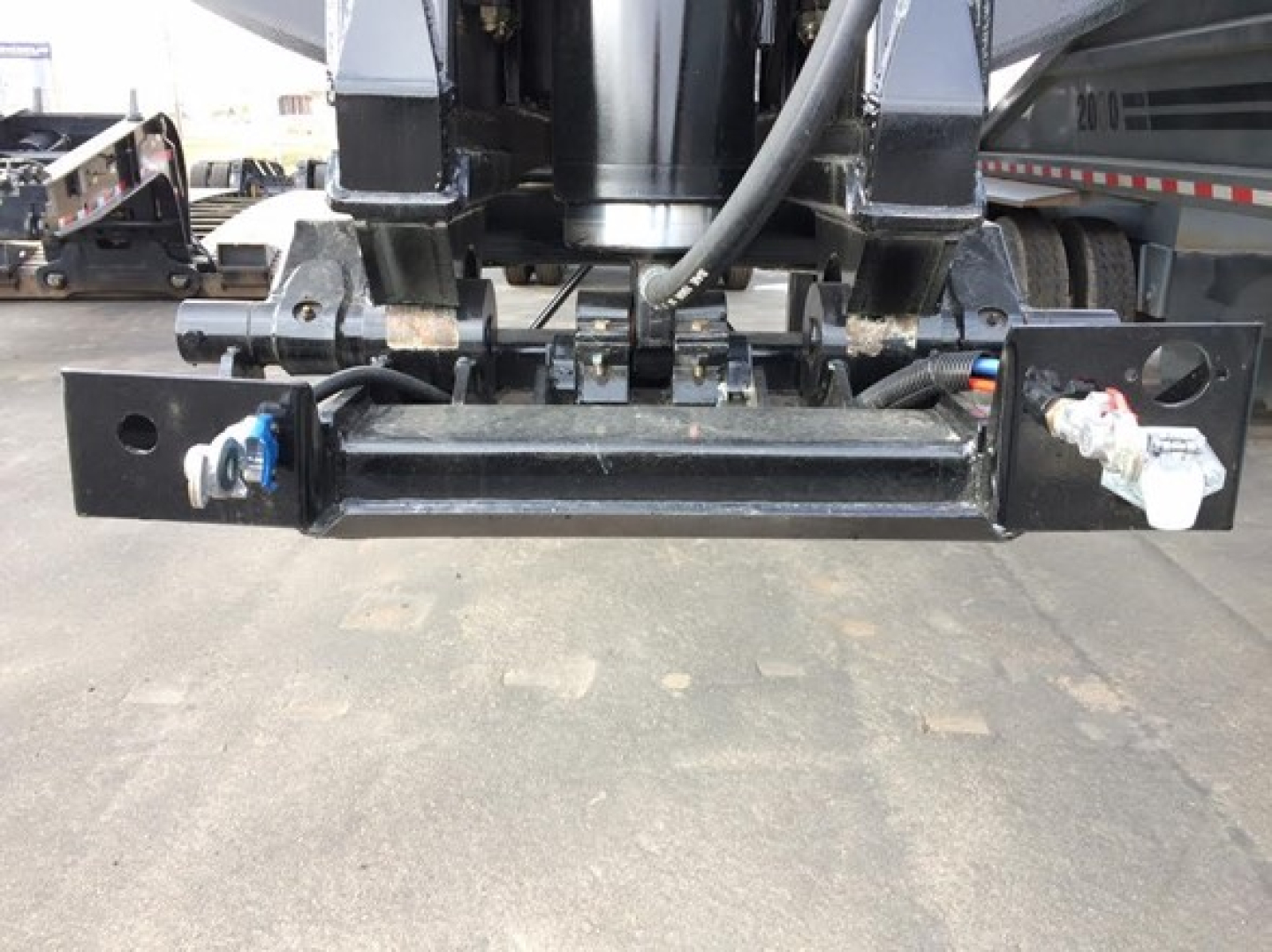 Dump trailer hitch/undercarriage showing hydraulic or pneumatic lines and mounting bracket with fittings.