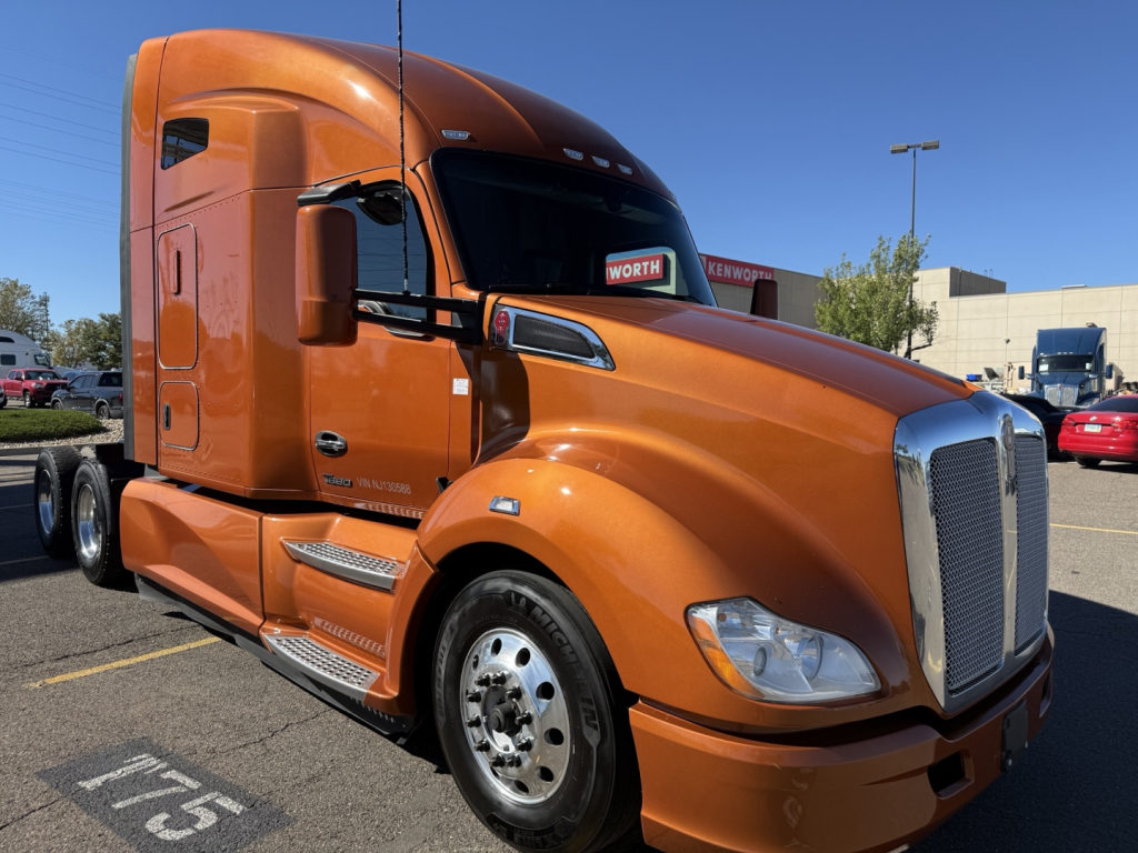 Kenworth T680 in orange, front-left view showing sleeper cab, large grille, headlights, and chrome mirrors.