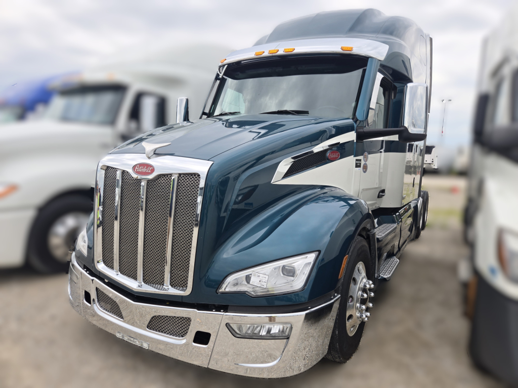 Peterbilt 579 conventional sleeper truck in blue with chrome grille and bumper, shown from front-left angle.