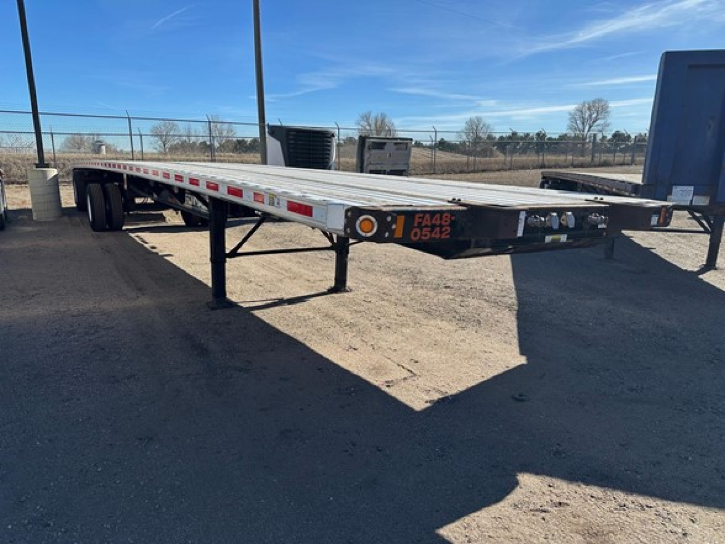 Flatbed trailer with lower deck and extended frame showing red reflective tape and FA48 numbers on the front end.