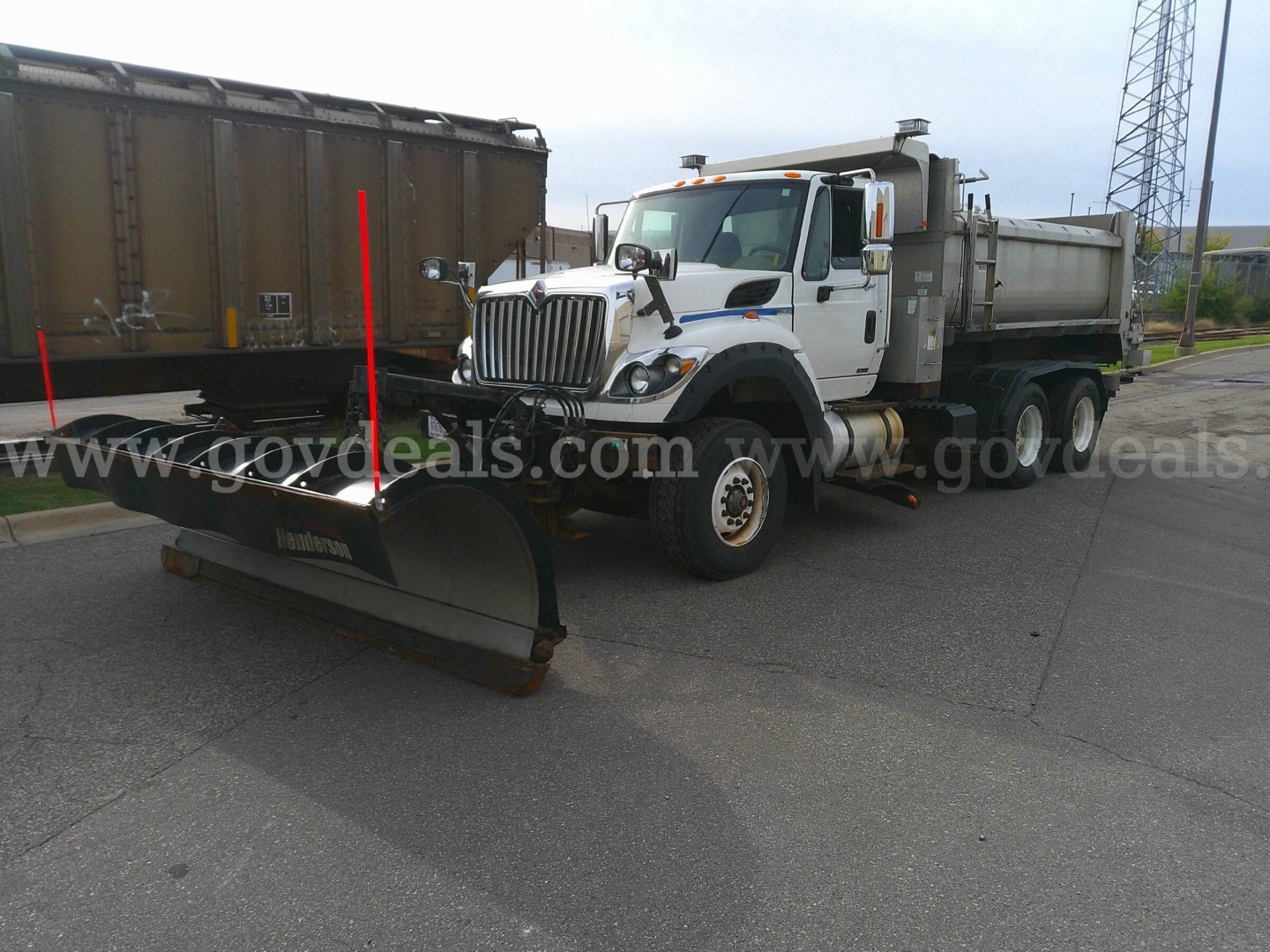 International WorkStar 7600 truck with plow attached, white cab, snow plow resting on front, dump body on back, on a paved lot.