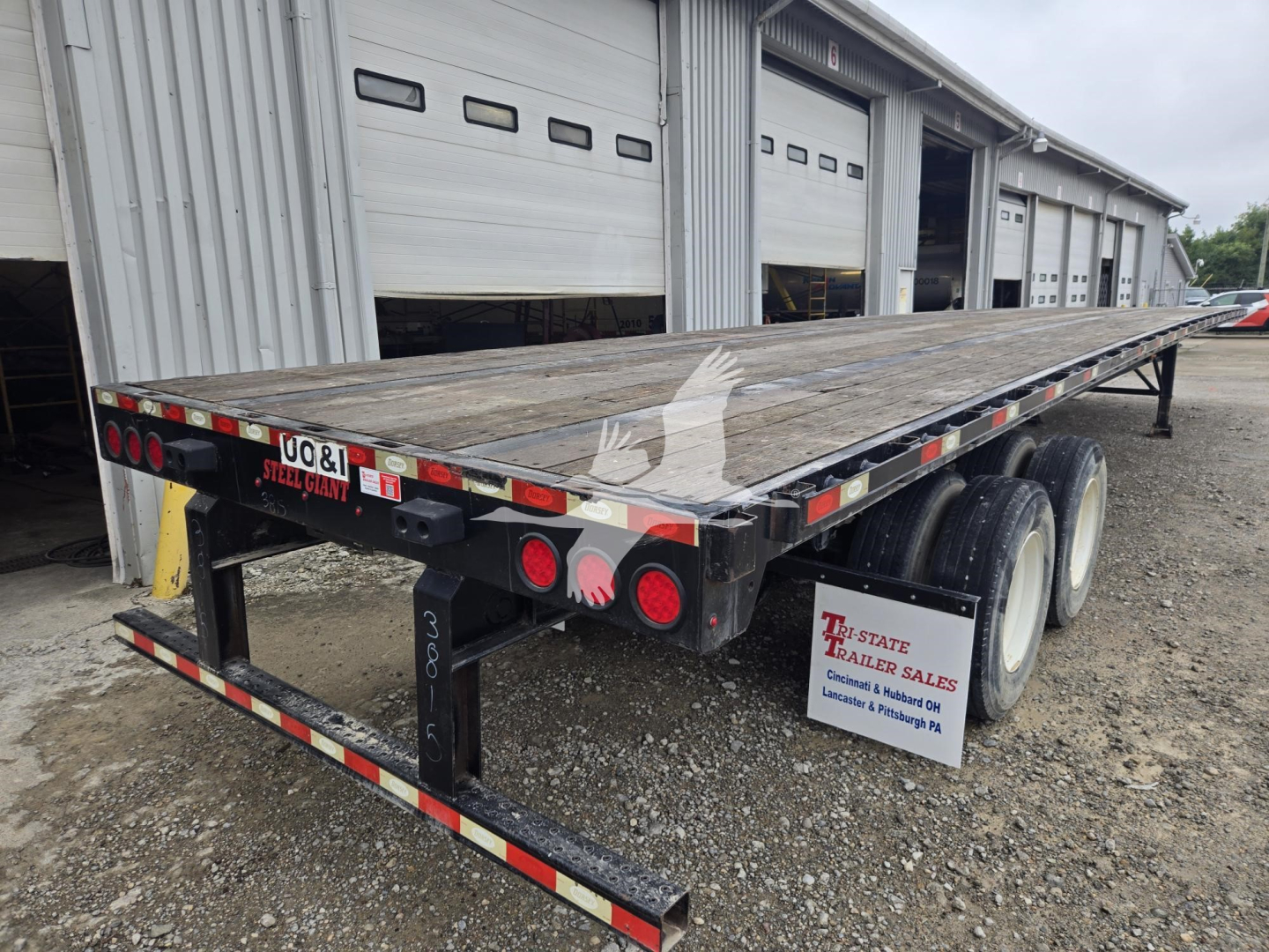 Trailer: 2018 Dorsey steel flatbed shown from rear-left side with dual rear axles and wood deck; outfitted with taillights, reflectors, and a black framed undercarriage.