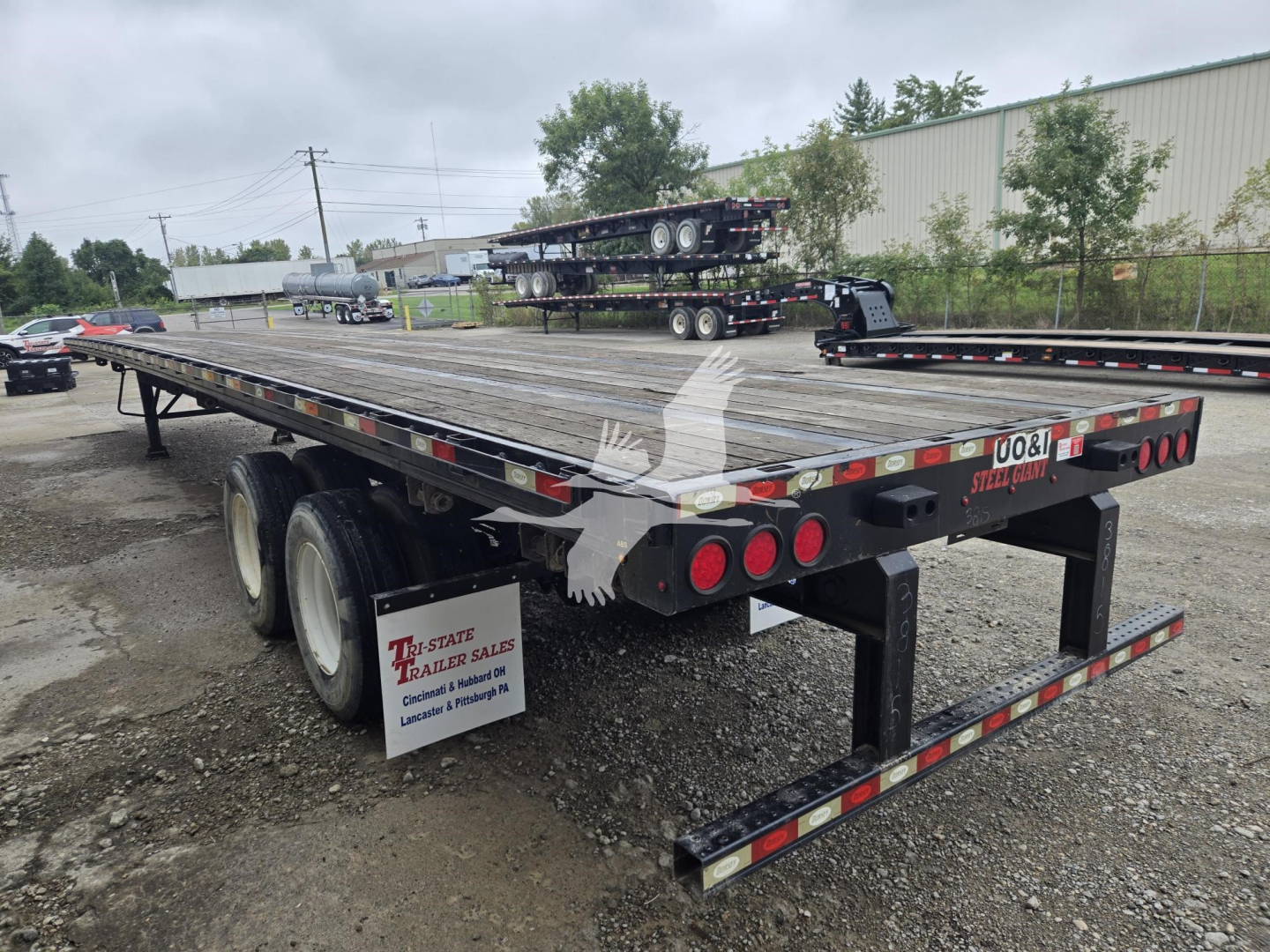 Flatbed trailer showing dual rear axles and deck planks, with taillights and reflective tape.