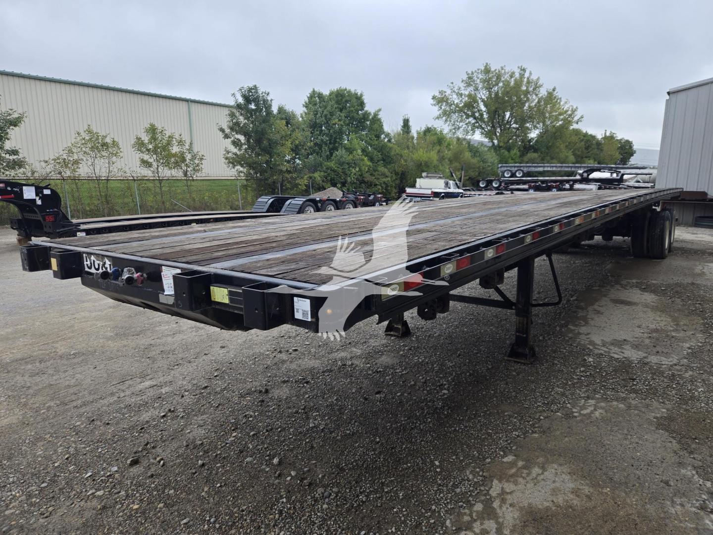 Flatbed trailer showing wooden deck with stake pockets and tandem axles in a yard.