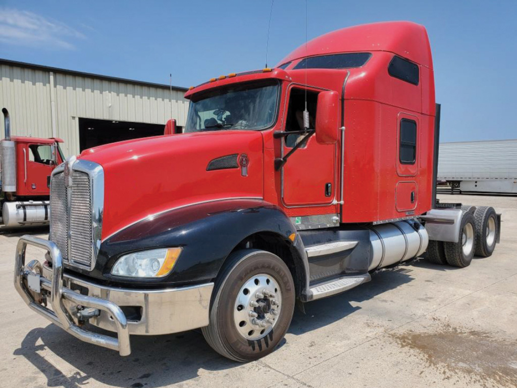 Kenworth T-660 aero cab tractor, red with chrome bumper and black fenders, side view showing diesel tanks and sleeper cab, 3-axle truck in a yard.
