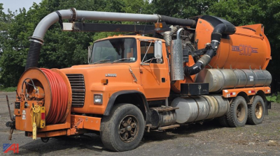 Ford LNT9000 vacuum tank truck with orange cab and Vactor 2100 system, hose reel on front bumper and large exhaust/filtration piping along side.