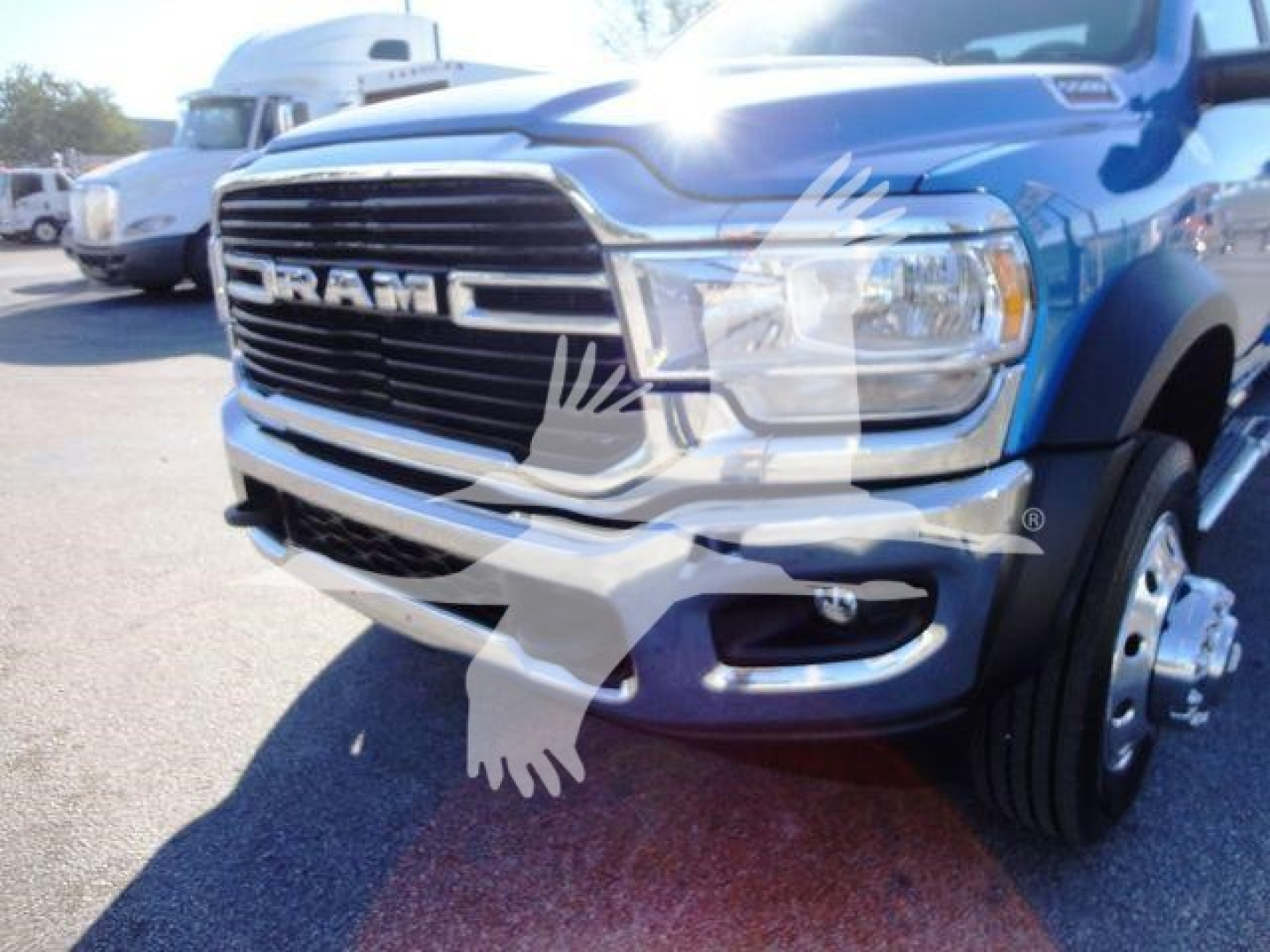 Ram truck front view showing grille with RAM lettering and partial bumper; wheel and tire visible; watermark of a bird in the center.