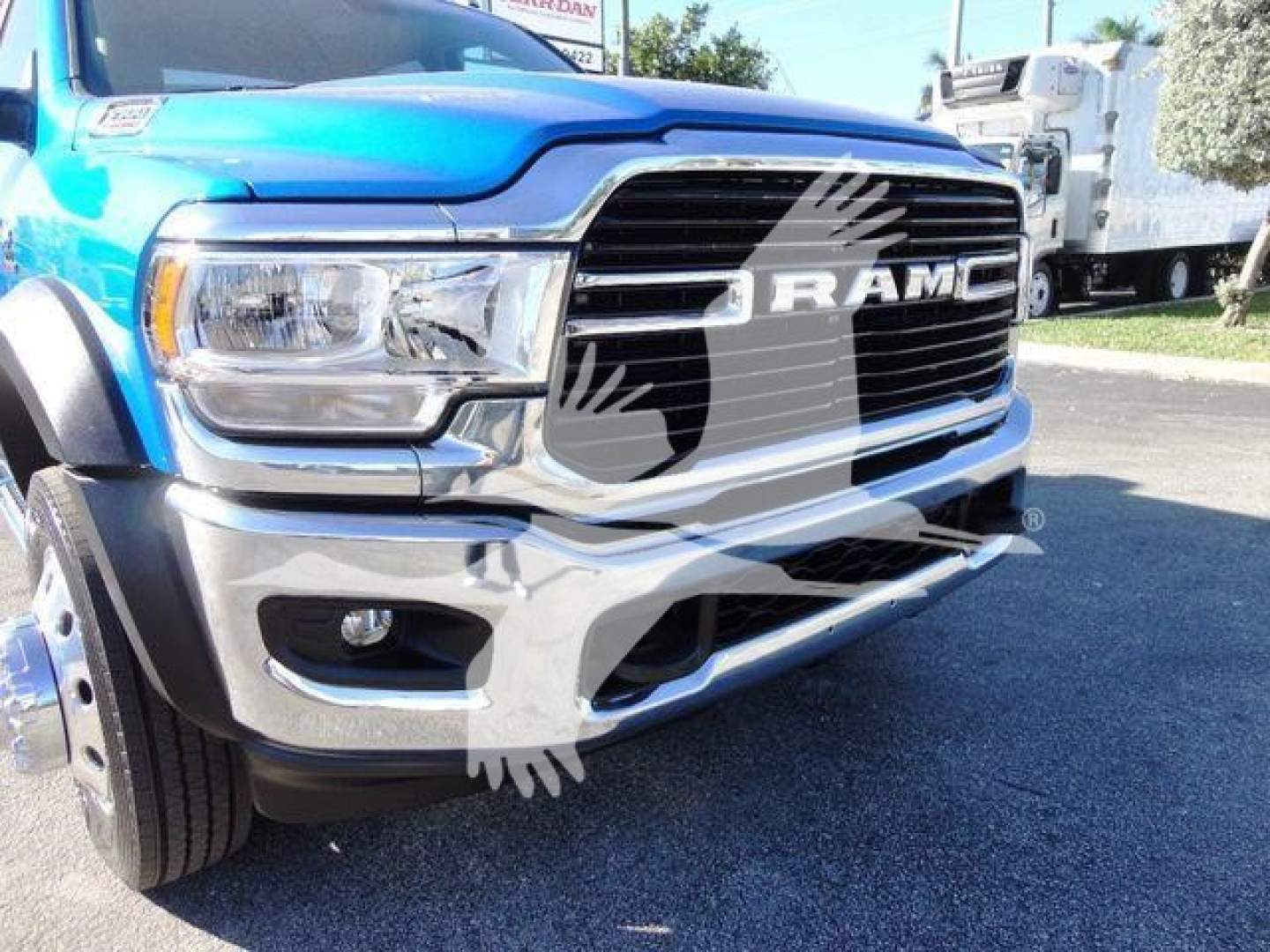 Ram 5500 front view showing bold grille with RAM letters and chrome bumper; blue pickup with partial wheel and fender visible.