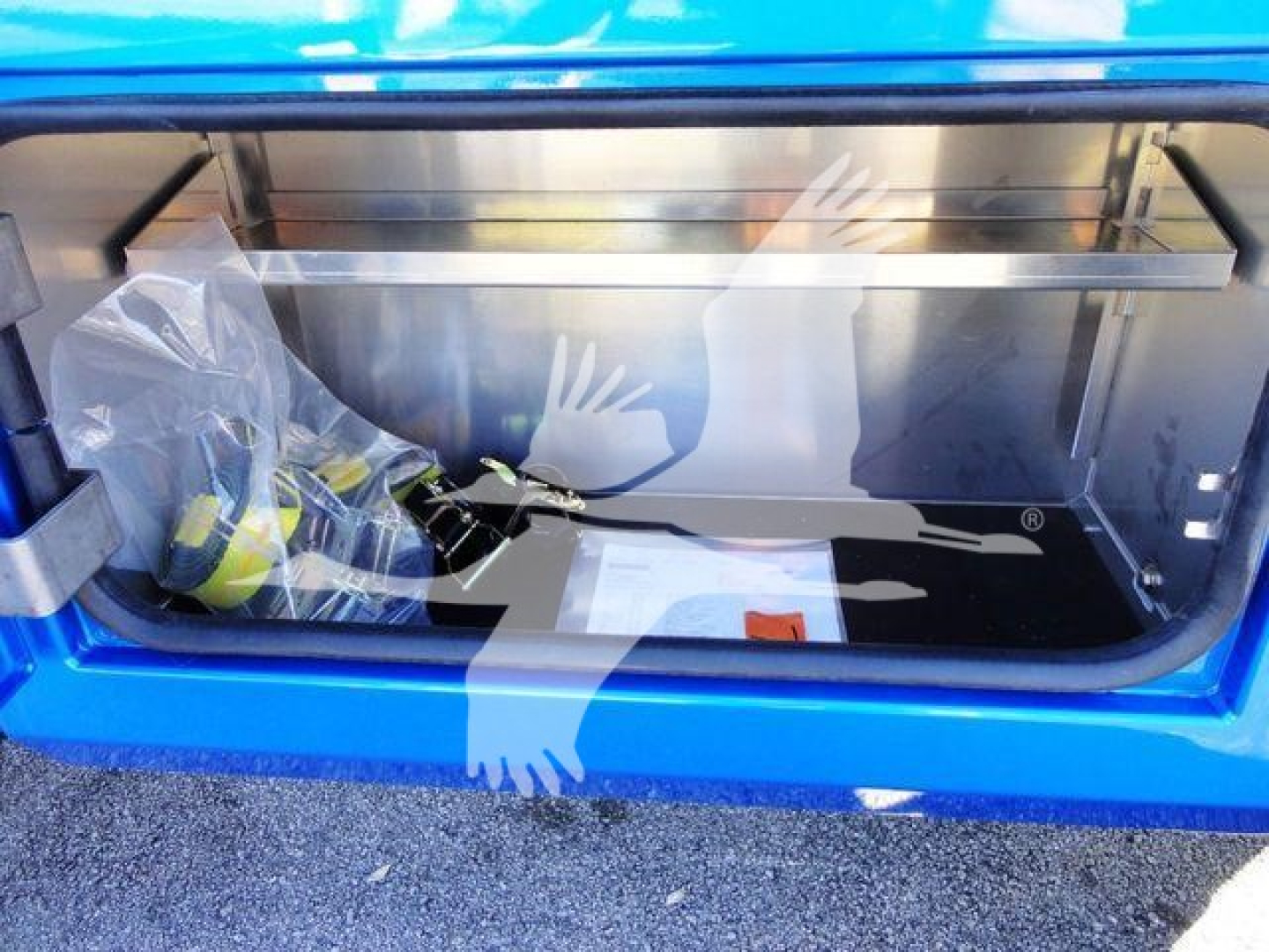 Trunk/storage compartment of a blue Ram pickup showing a winch area with packaging and tools inside, metal frame and reflective surfaces.