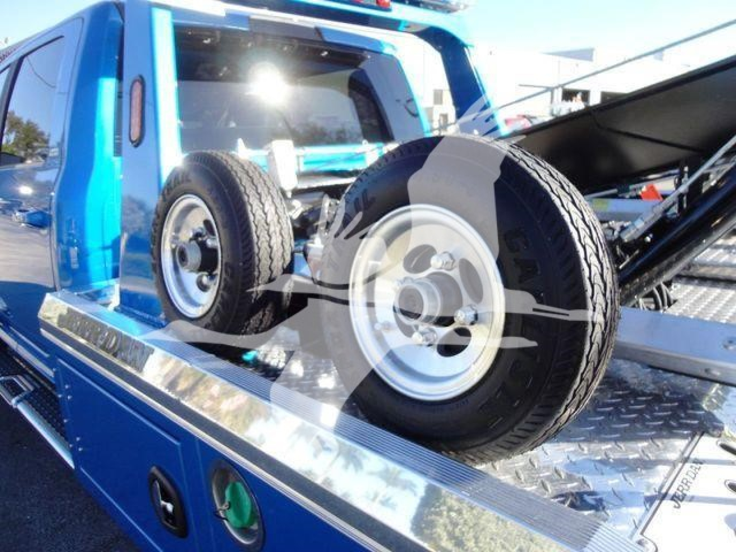 Ram 5500 truck on a tow bed with a spare tire mounted on the deck and bright blue bodywork visible.