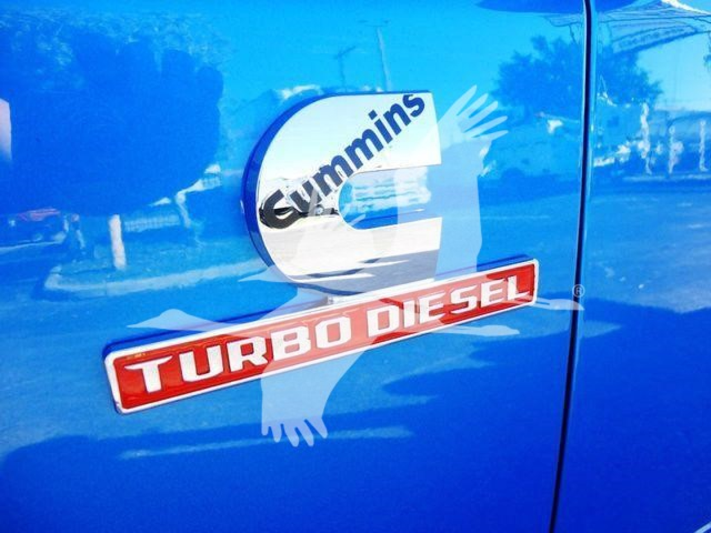 Door panel showing Cummins turbo diesel badge and RAM truck emblem on blue pickup side.