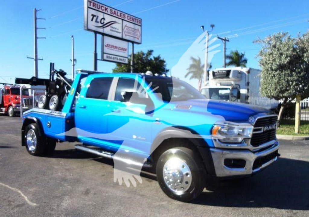 Blue 2024 Ram 5500 SLT tow truck with front chrome grille, winch equipment on bed, large dual rear wheels, showroom lot in background.