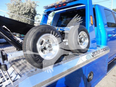 Ram 5500 SLT tow truck bed with wheels and spare tires on a blue truck, JER K. DAN branding on side, front windshield and equipment rack visible.