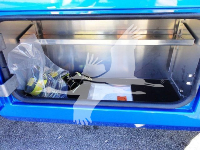 Trunk/storage compartment of a blue Ram pickup showing a winch area with packaging and tools inside, metal frame and reflective surfaces.