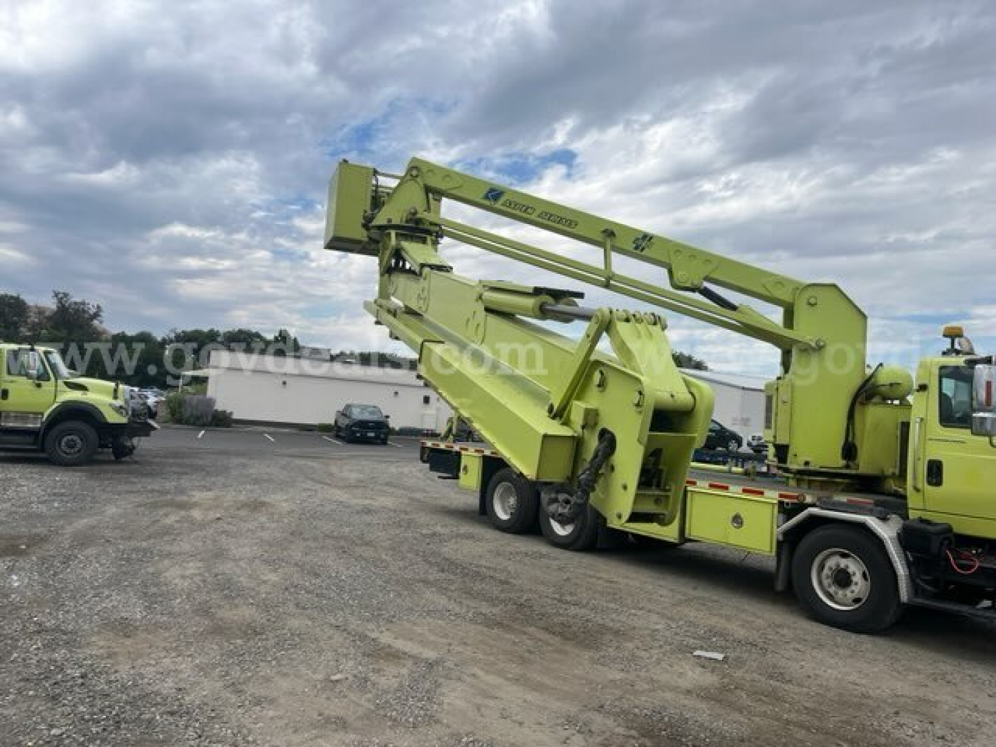 Boom truck with green articulating crane mounted on dual rear-axle chassis and a bucket at the end; International 7600 bucket truck yard rig.